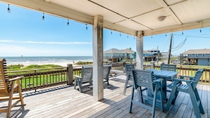 A wooden deck with outdoor seating, overlooking a beach and ocean.
