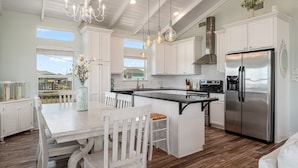 A modern kitchen with white cabinetry, a stainless steel refrigerator, and a dining area with a white table and chairs.