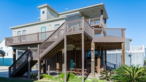 Ein zweistöckiges Haus mit überdachter Terrasse, Sitzgelegenheiten im Freien und einer Treppe, die zum oberen Stockwerk führt.