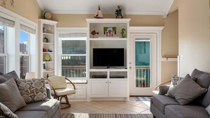Ein Wohnzimmer mit Fernseher, weißem Unterhaltungsschrank, grauen Sofas und einem Balkon mit Ausblick.