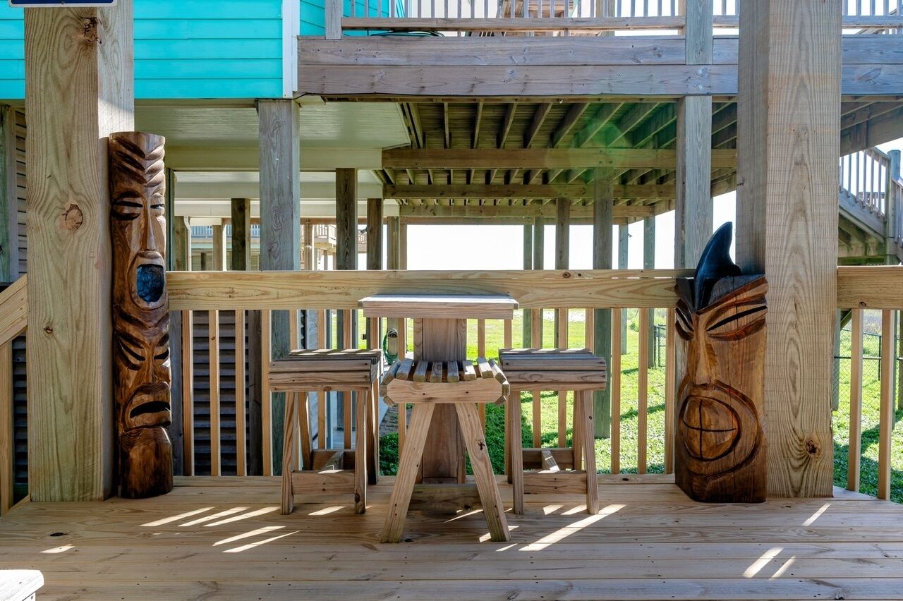 Een houten terras met een tafel en stoelen, omringd door houten leuningen en twee houten sculpturen.