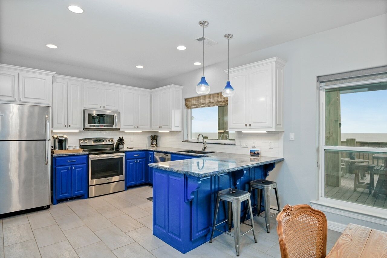 A modern kitchen with white cabinets, blue accents, stainless steel appliances, and a large island with stools.