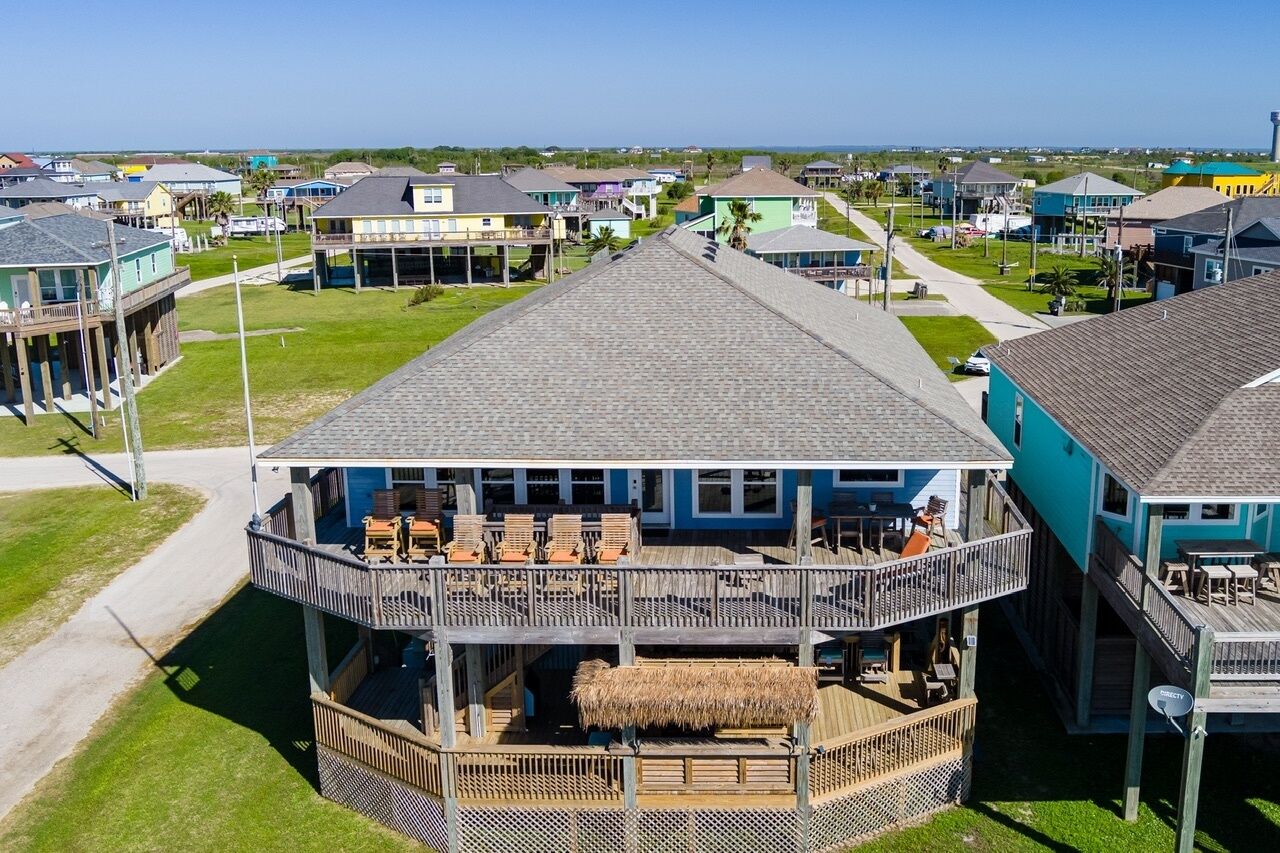 A beachfront property with a two-story building featuring a balcony with outdoor seating and a thatched roof.