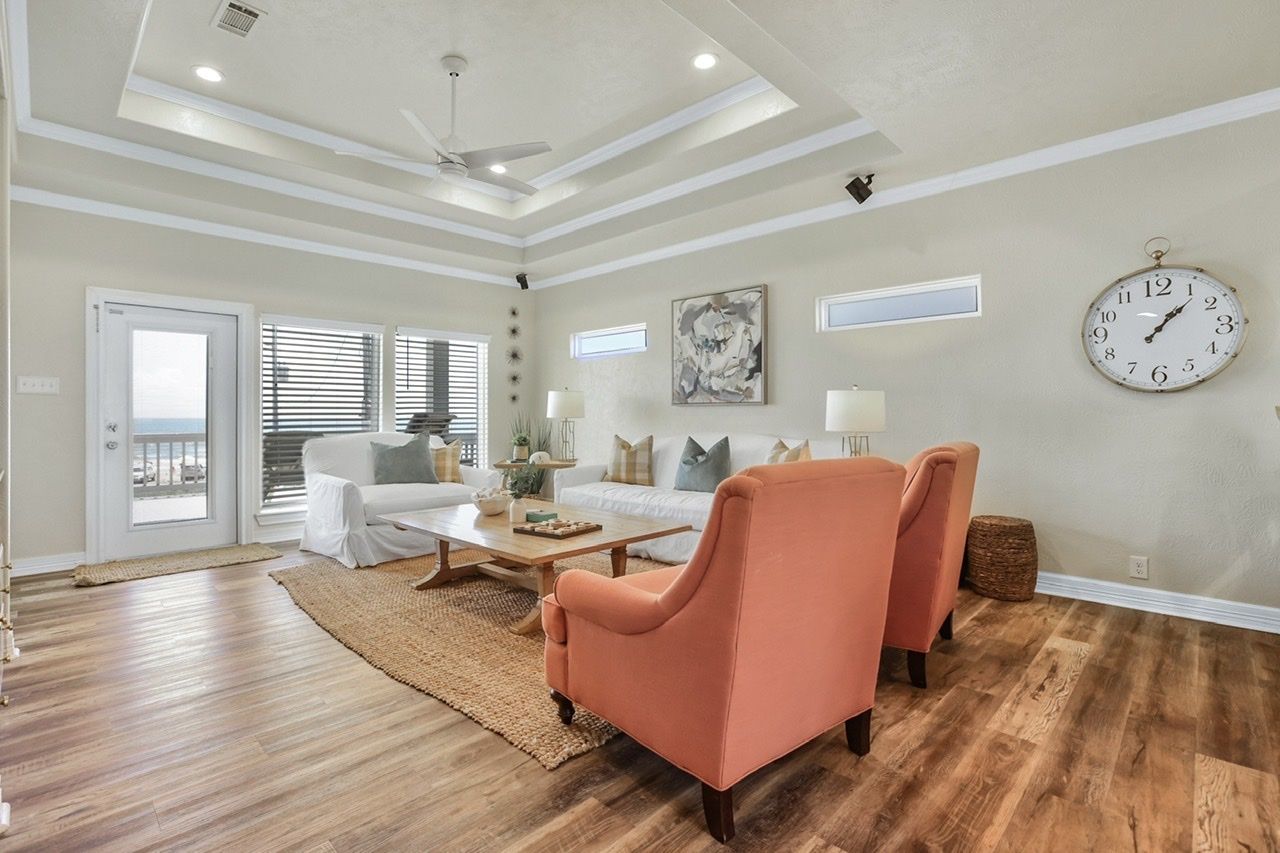 A spacious living room with a large clock, a ceiling fan, and a view through the glass doors.