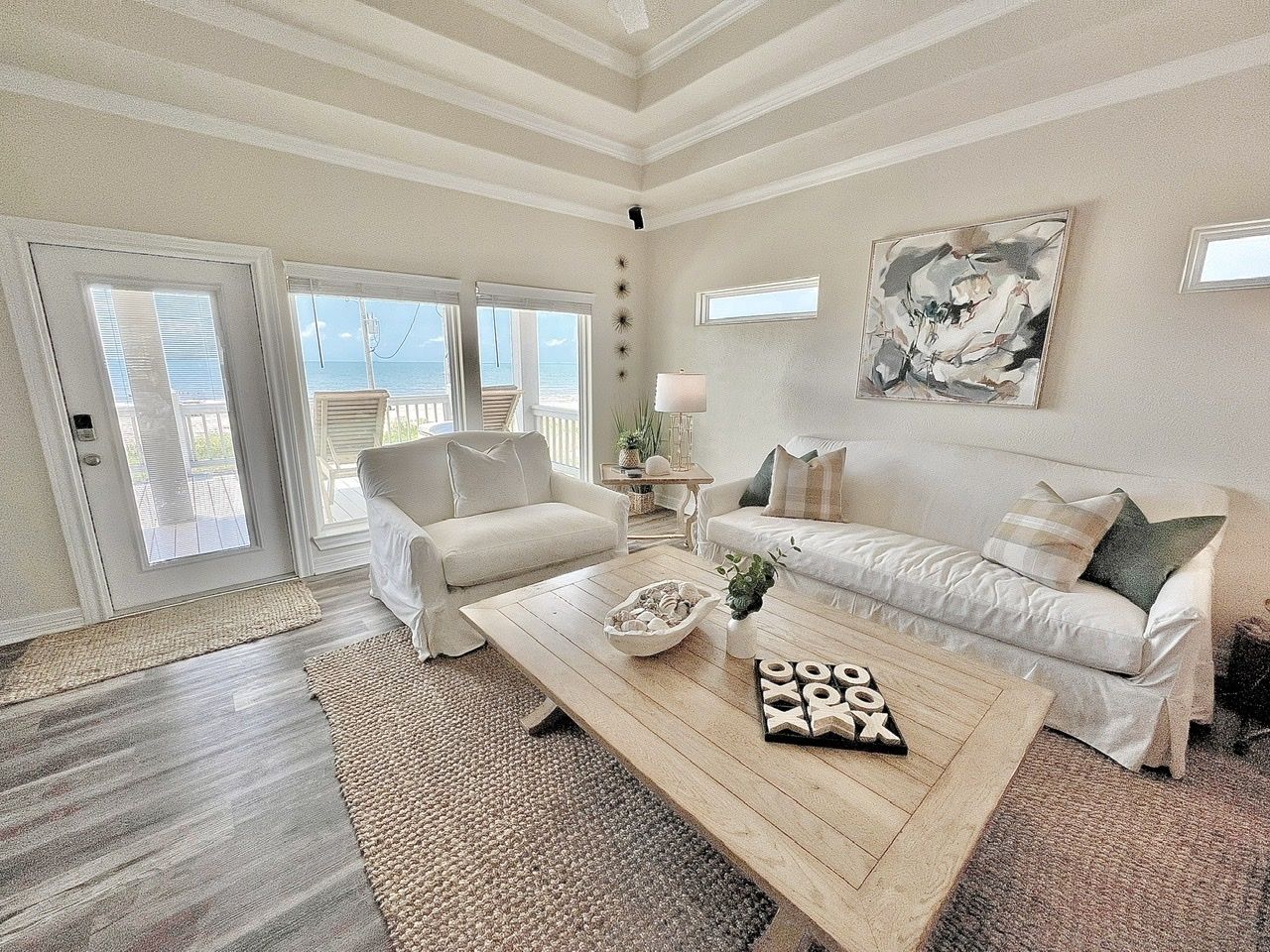 A spacious living room with a large wooden coffee table, two white sofas, and a view of the ocean through large sliding glass doors.