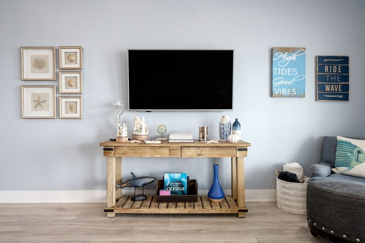 A living room with a wooden console table, a flat-screen TV, framed pictures, and a motivational sign.