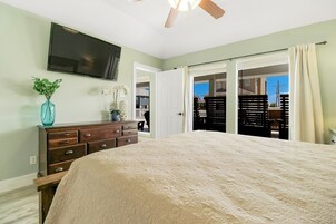 A bedroom with a large bed, a dresser, a TV on the wall, and a sliding door leading to a balcony.