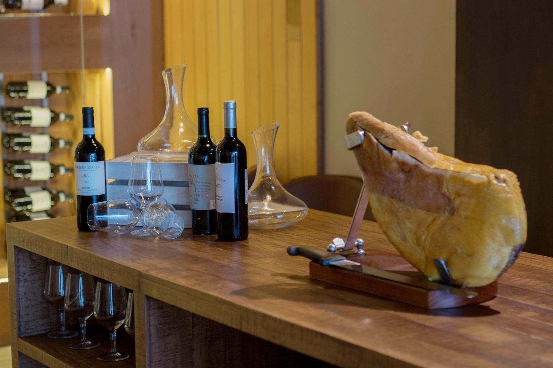 A bar area with wine bottles, glasses, and a large meat carving.