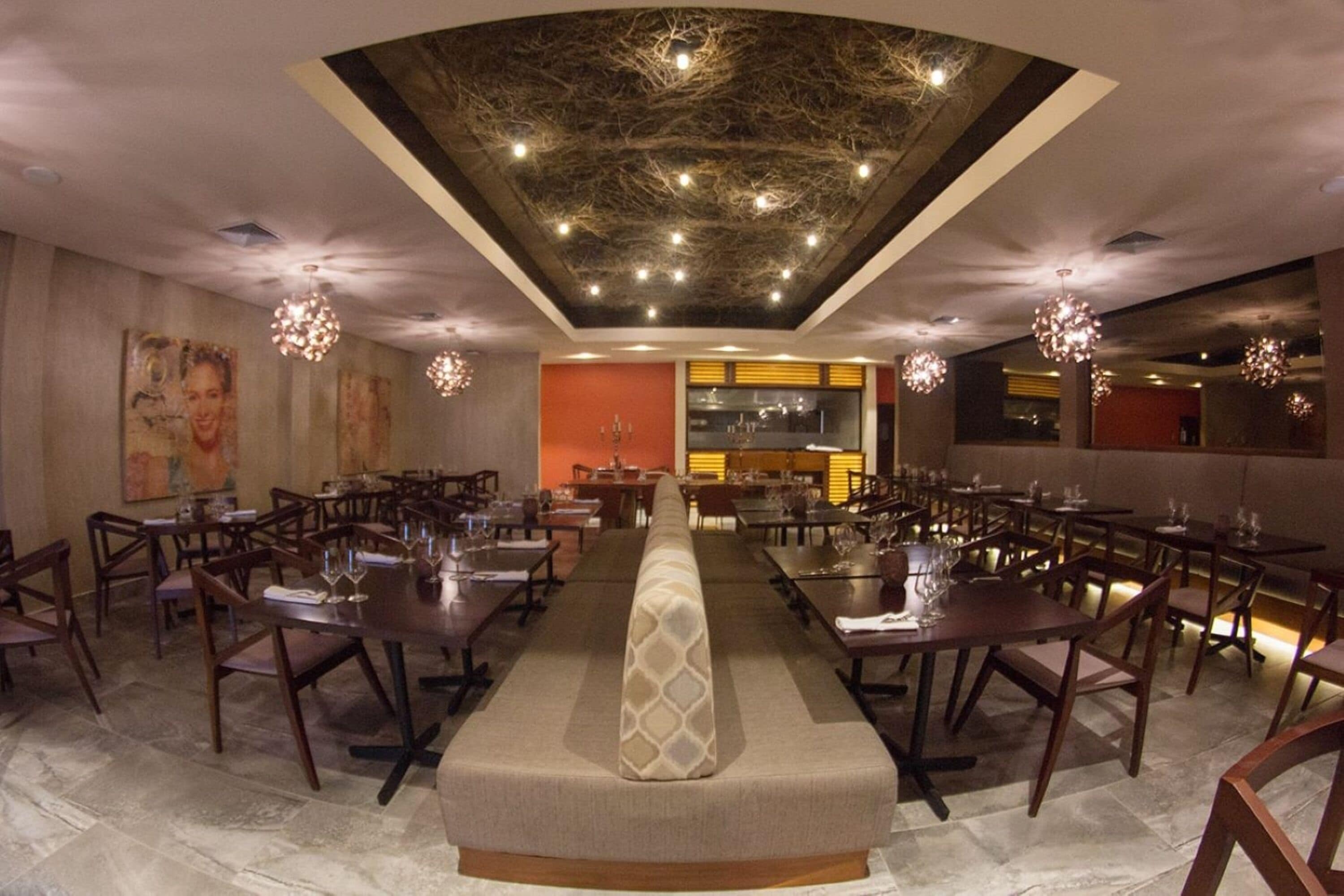 A spacious dining area with multiple tables and chairs, a central seating area, and decorative lighting fixtures.