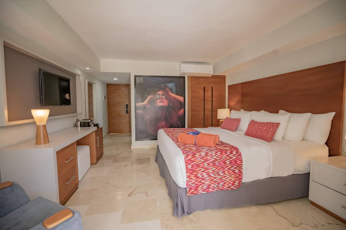 A modern hotel room with a large bed, a desk, a TV, and a bathroom visible through an open door.