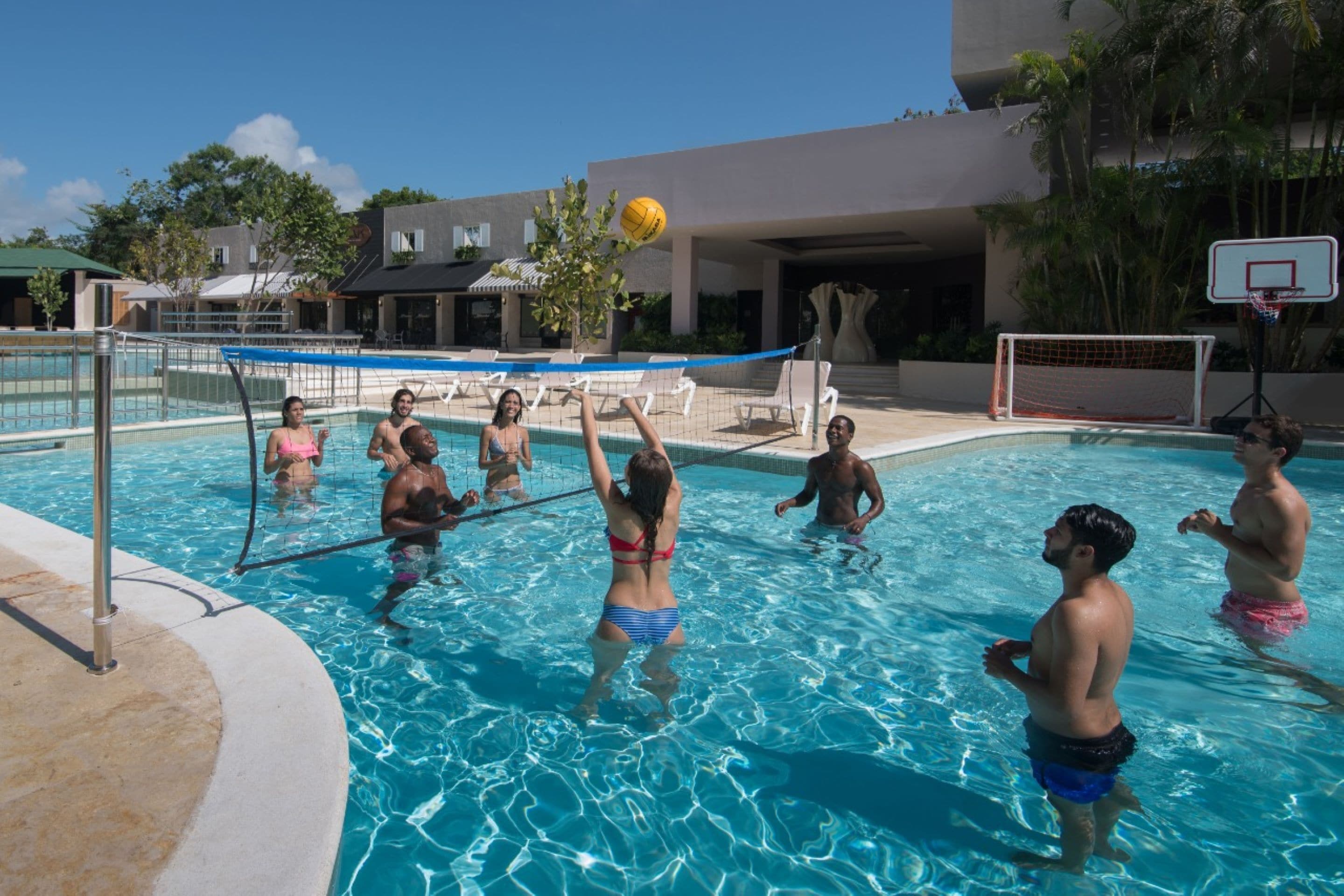 Ein Schwimmbeckenbereich mit Volleyballnetz, Liegestühlen und Basketballkorb.