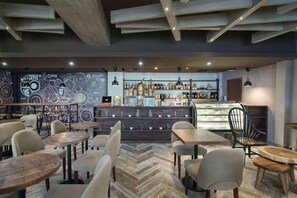A modern cafe interior with wooden tables and chairs, a coffee bar, and a herringbone-patterned floor.