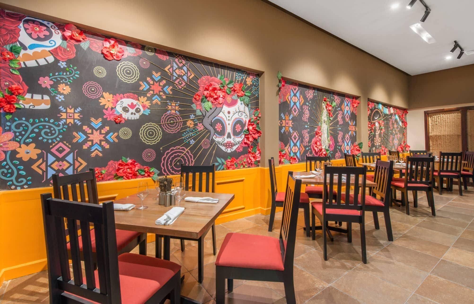 A restaurant with tables and chairs, decorated walls with colorful patterns, and a tiled floor.
