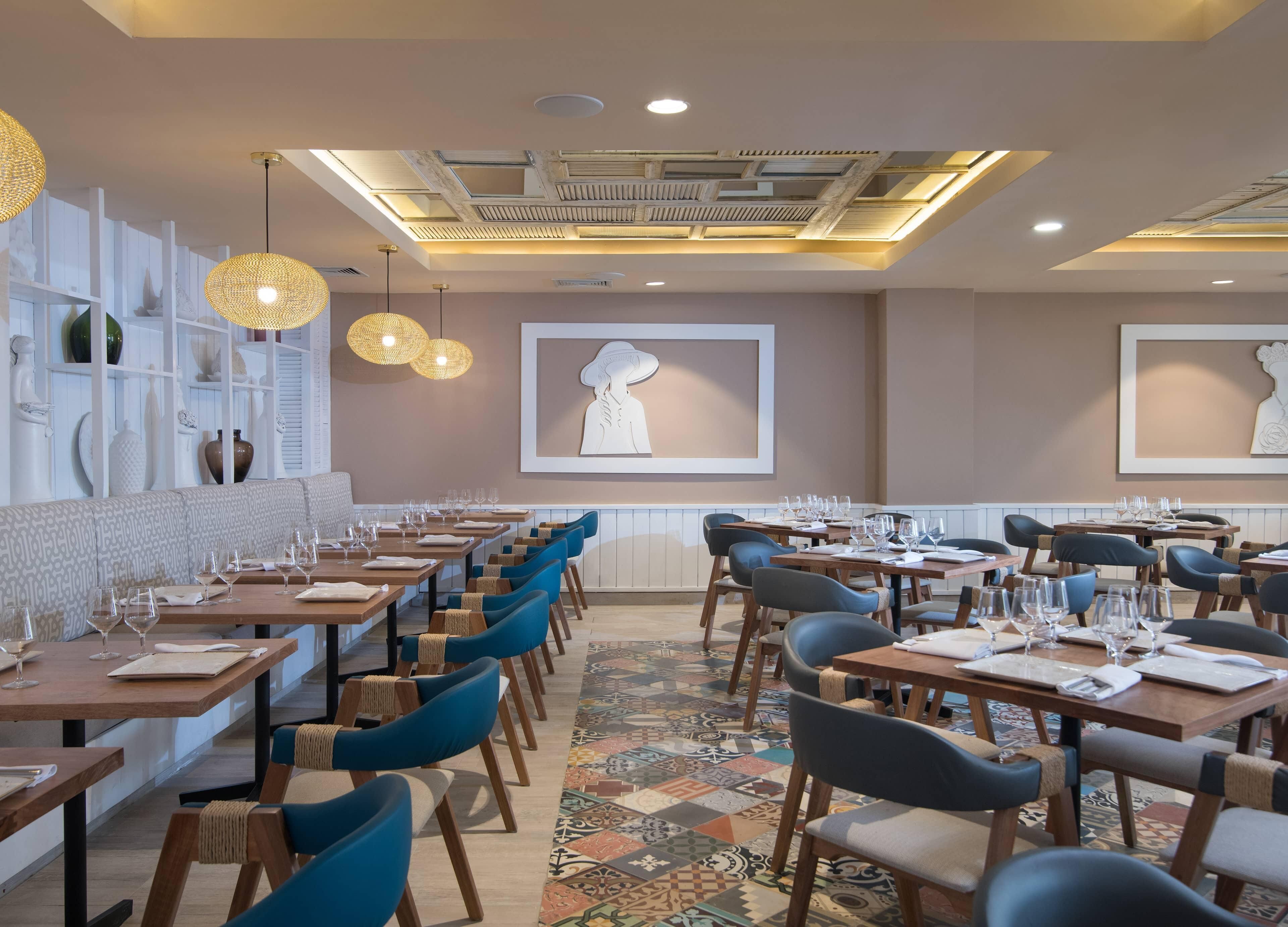 A restaurant with multiple dining tables, blue chairs, and a patterned floor.