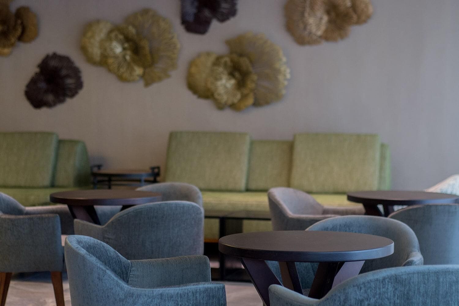 A modern lounge area with green sofas and blue armchairs, featuring a wall with decorative, textured wall art.