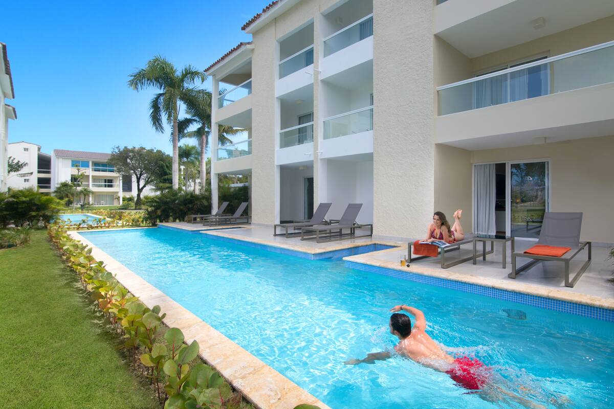 A swimming pool with lounge chairs and a building with balconies.