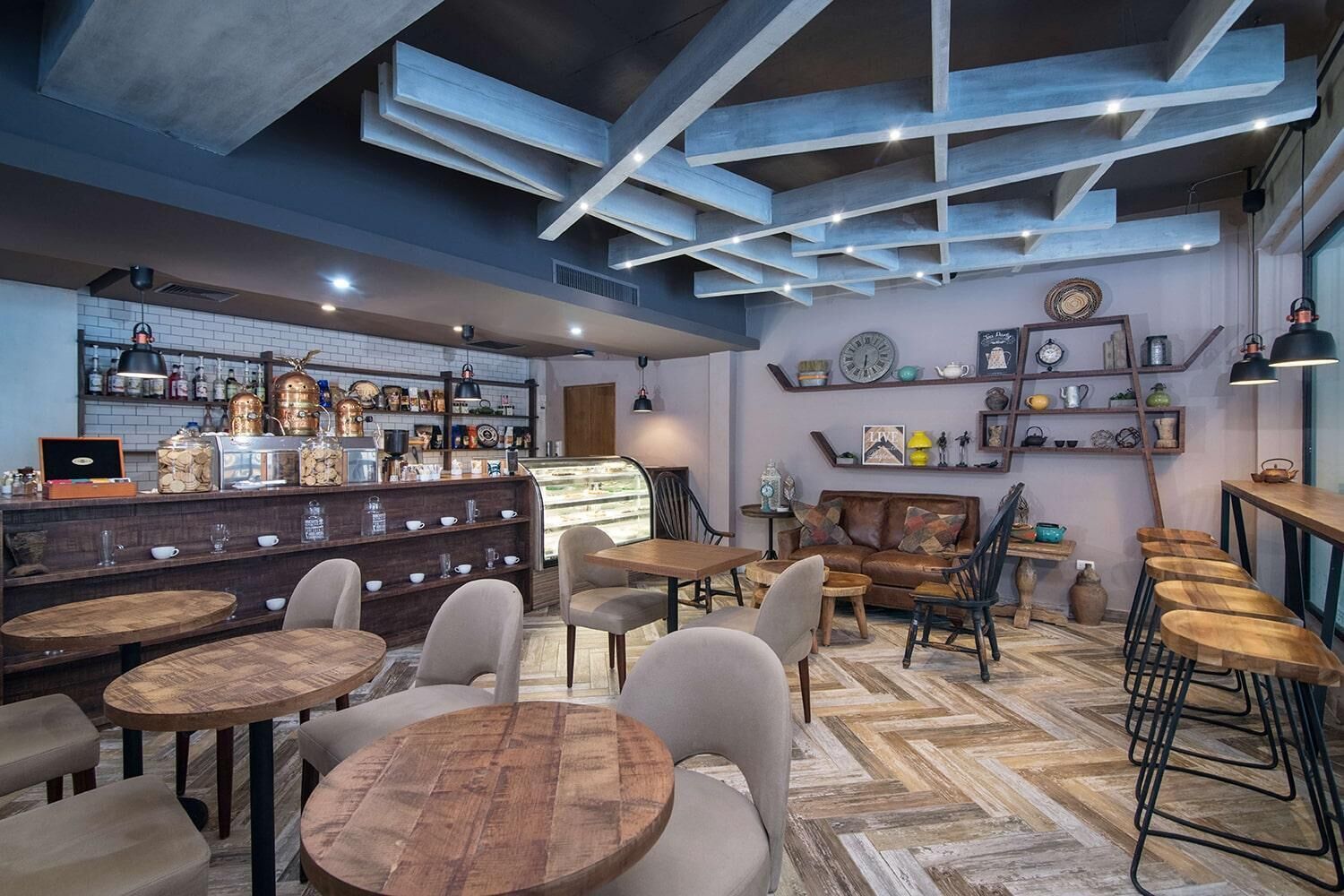 Un cafè acollidor amb taules i cadires de fusta, una zona de bar amb prestatges plens de botelles i un sostre decoratiu.