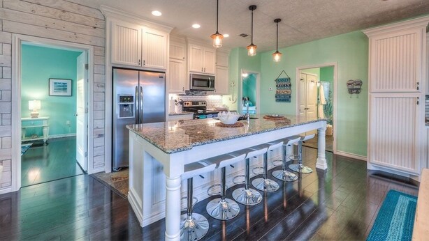 A spacious kitchen with white cabinetry, a central island with bar stools, and pendant lighting. - Once Upon A Tide 3 Bedroom Home by RedAwning (Port Bolivar)