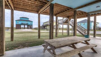 A covered outdoor area with a picnic table, wooden beams, and a view of houses in the background.