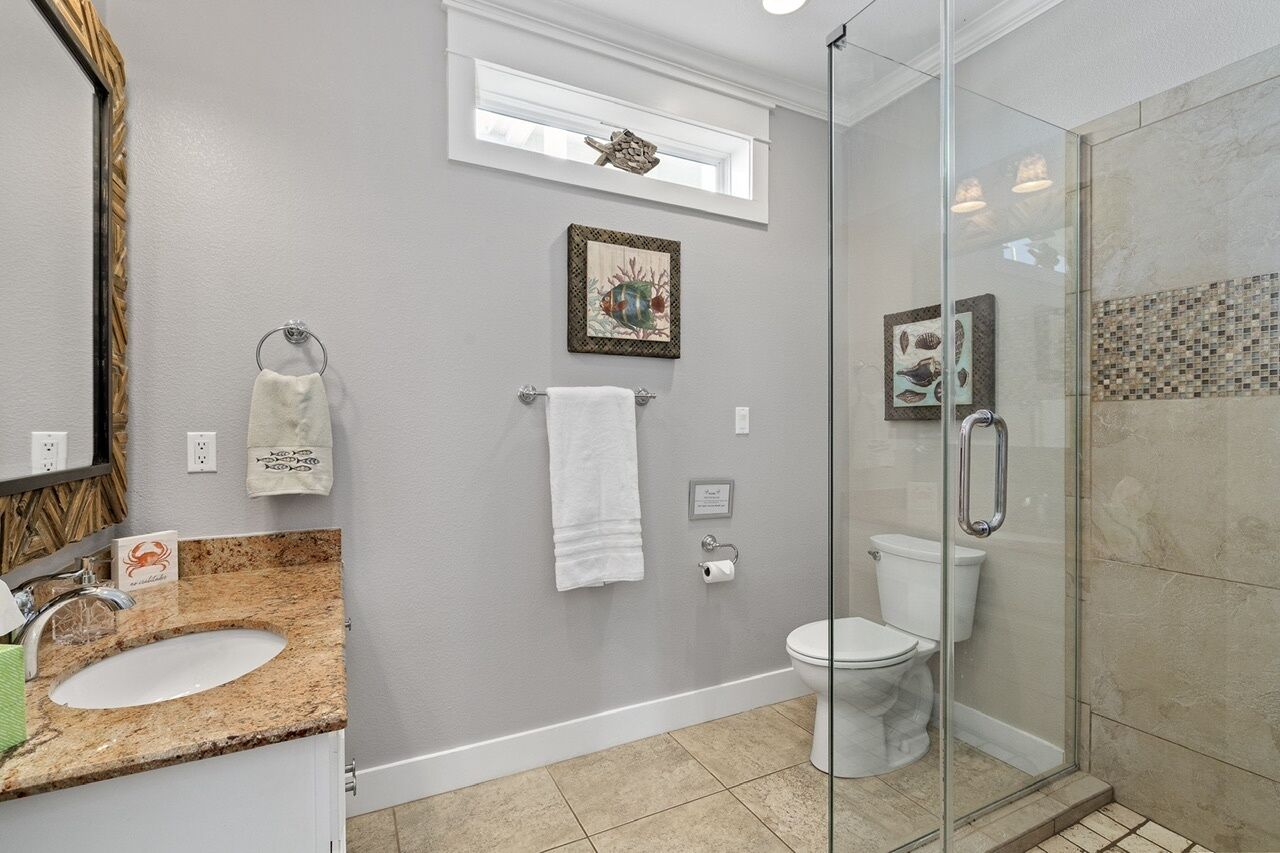 A bathroom with a granite countertop sink, a glass shower enclosure, and a white toilet.