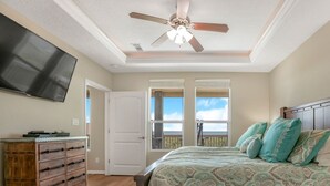 A bedroom with a bed, a ceiling fan, a TV, a dresser, and a window with a view.