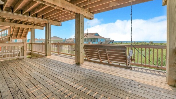 A wooden deck with a swing, a railing, and a view of the ocean and buildings in the background.