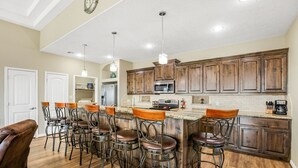 A spacious kitchen with wooden cabinets, a central island with bar stools, and a dining area with a brown leather chair.