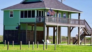 A two-story house with a balcony and a small deck, featuring a flag and a chair outside.