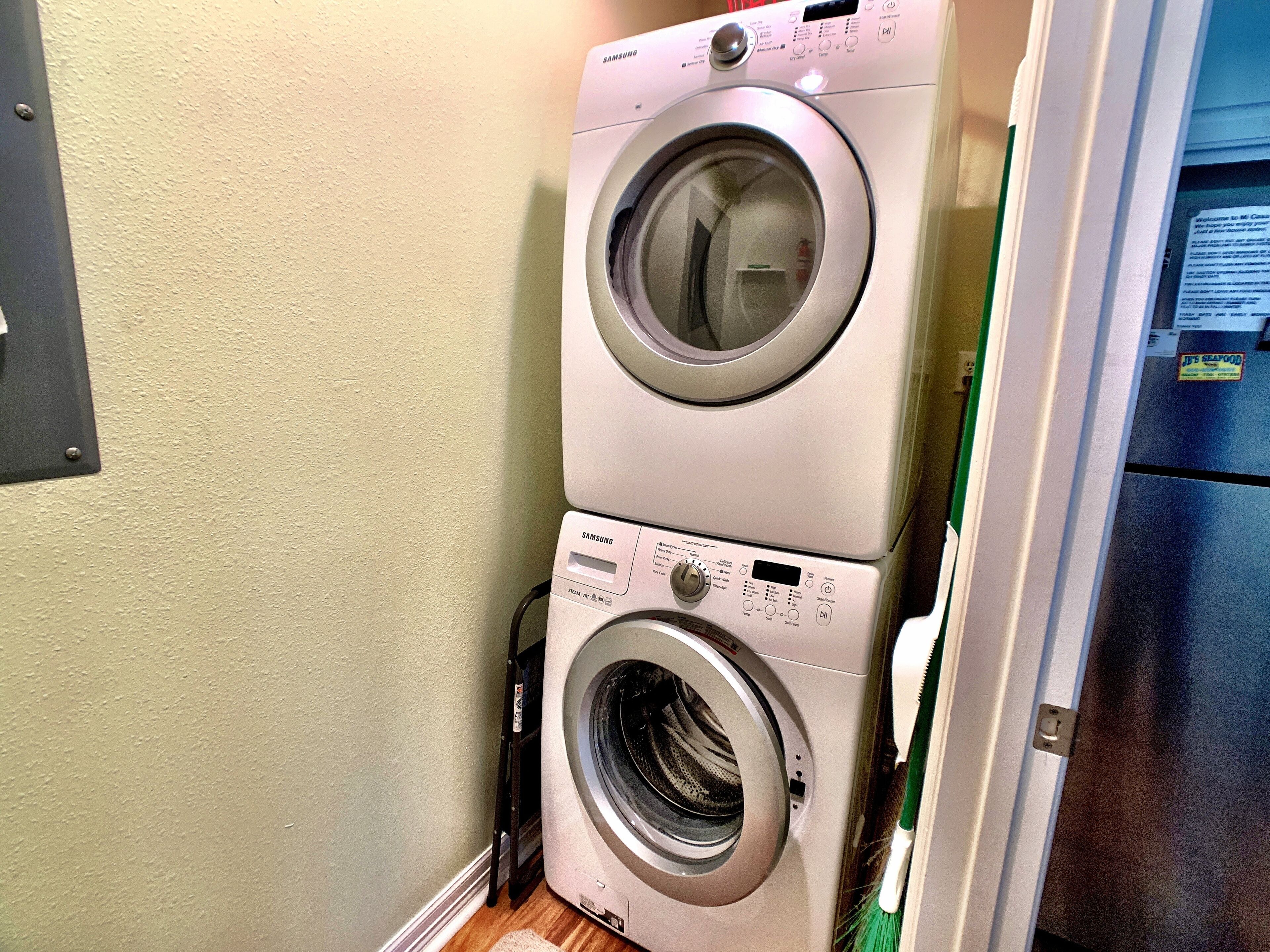 A stacked washer and dryer unit in a laundry room with a wooden floor and a green door frame.