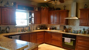 A kitchen with wooden cabinets, granite countertops, a built-in oven, and a window with a view. - The Sandy Cork 4 Bedroom Home by RedAwning (Port Bolivar)