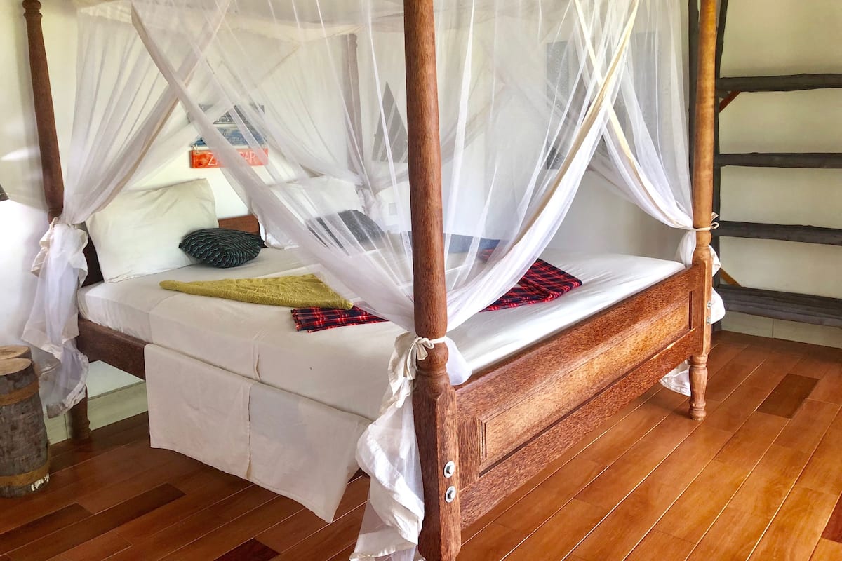 A four-poster bed with a canopy, wooden flooring, and a small bedside table.