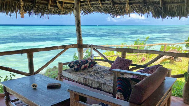 A wooden deck with a thatched roof overlooking turquoise waters. - Promised Land Lodge (Kizimkazi)