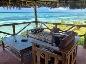 A wooden deck with a thatched roof overlooking turquoise waters. - Promised Land Lodge (Kizimkazi)