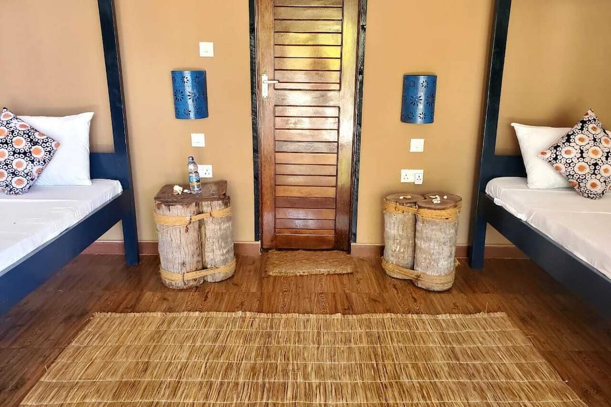 A room with two beds, a wooden door, and a woven rug.