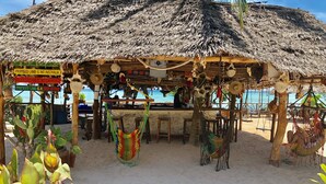 A beachside hut with a thatched roof, a bar area, and hanging hammocks. - Promised Land Lodge (Kizimkazi)