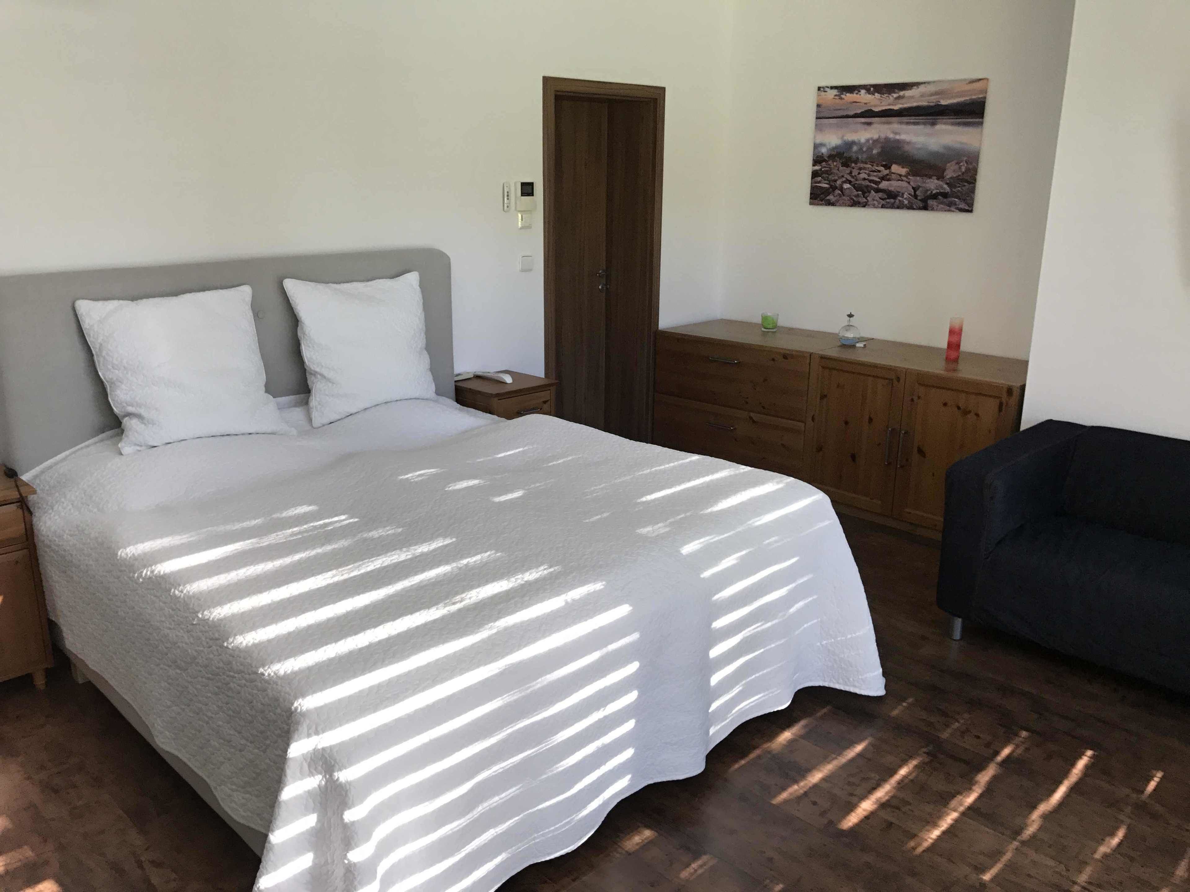Een slaapkamer met een bed, nachtkastje, dressoir en een stoel.