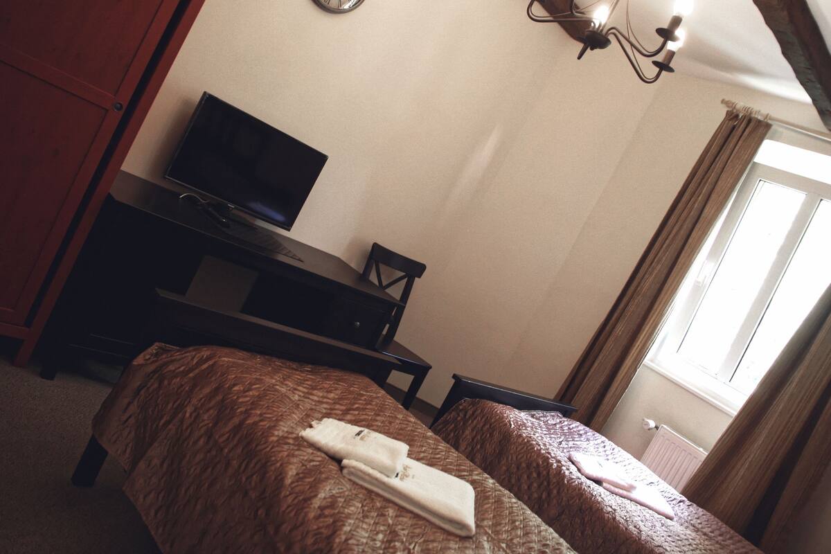 A hotel room with two beds, a TV, a desk, and a window with curtains.