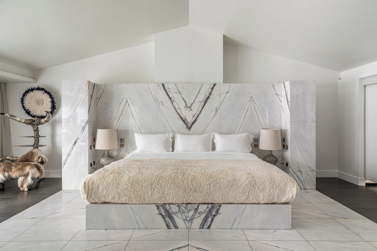 A modern bedroom with a large bed, marble headboard, and a decorative wall piece.