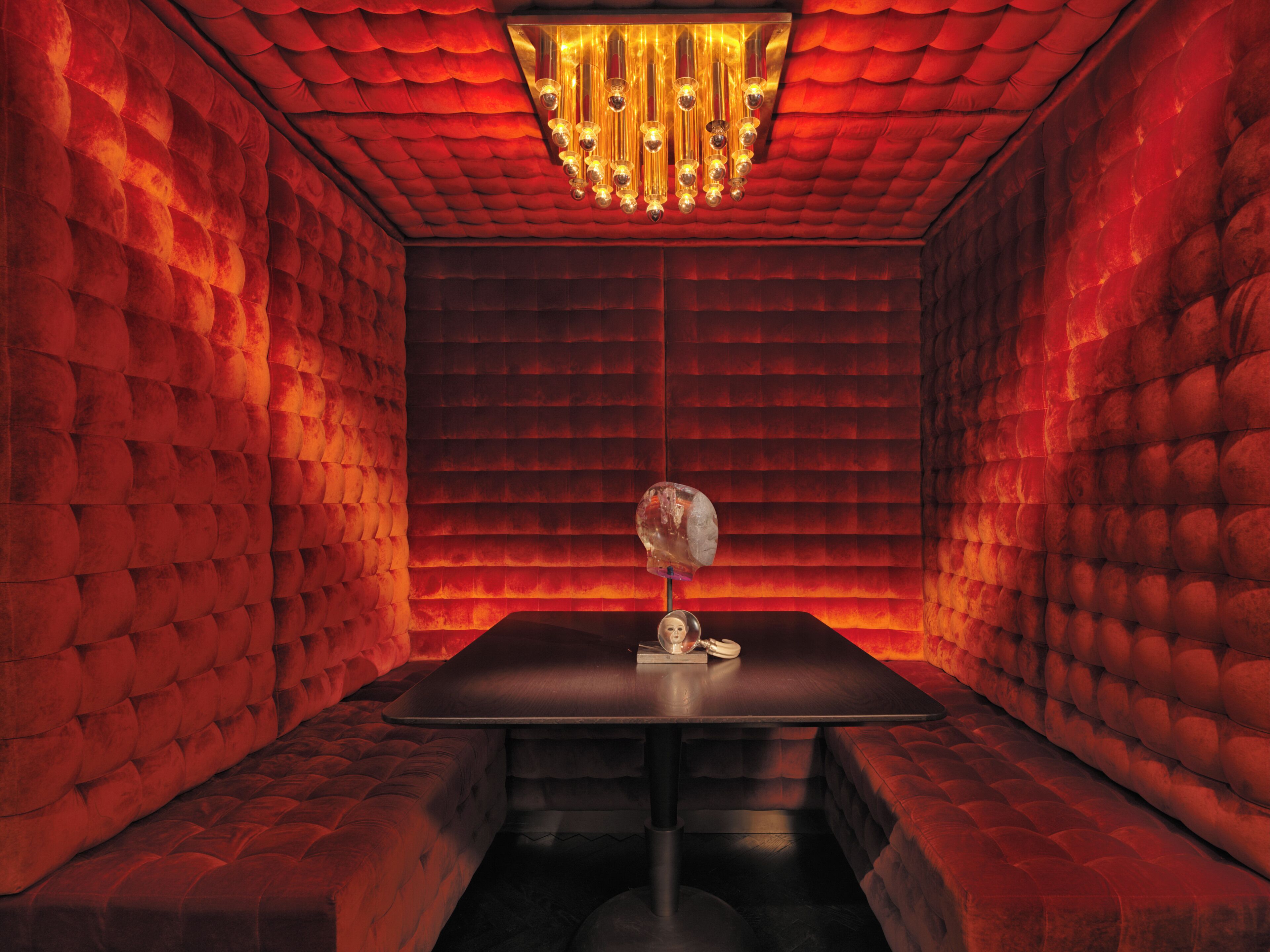 A room with a red brick wall, a chandelier, and a table with a mirror.