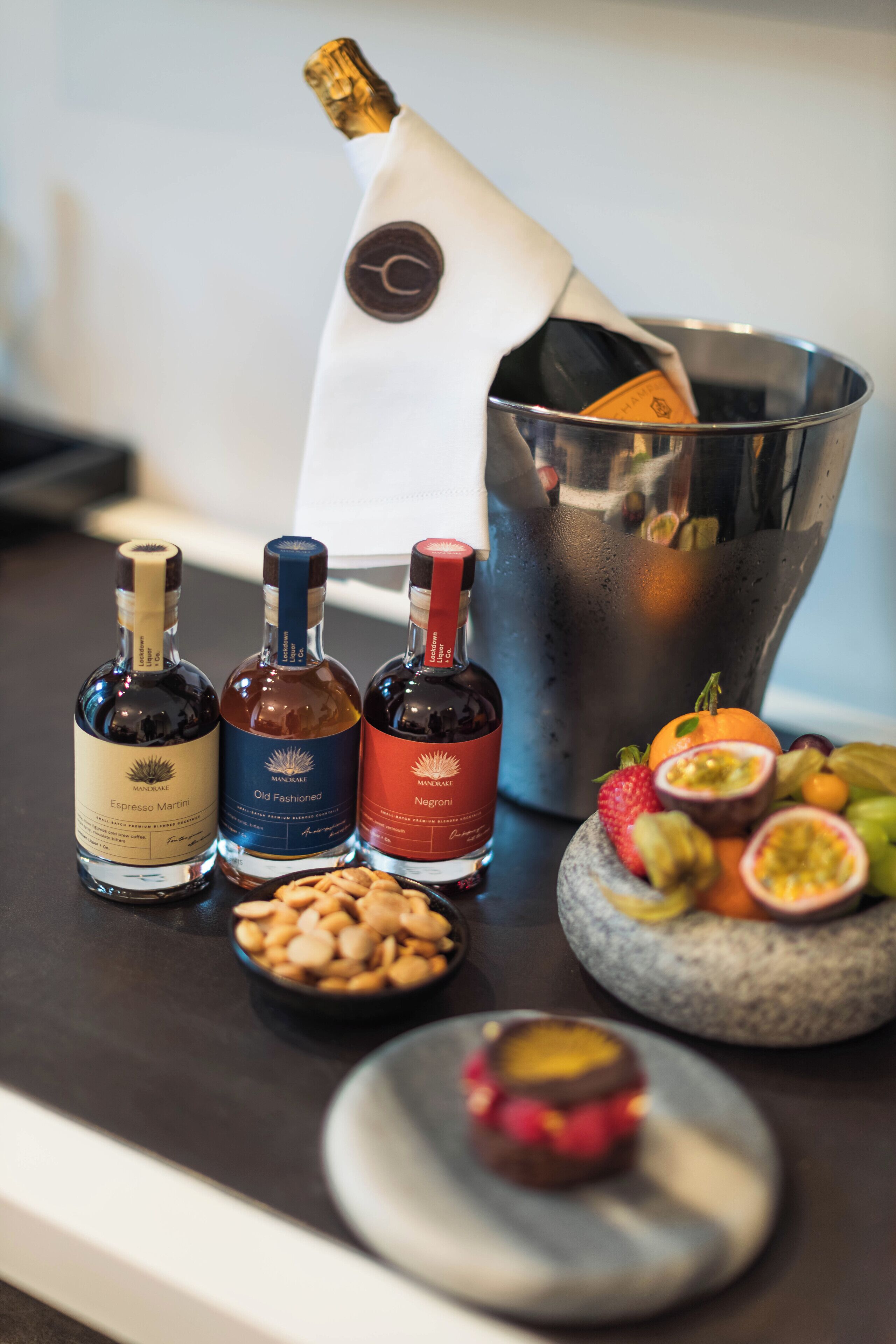 A selection of liquor bottles, a champagne bottle, and a variety of fruits on a table.