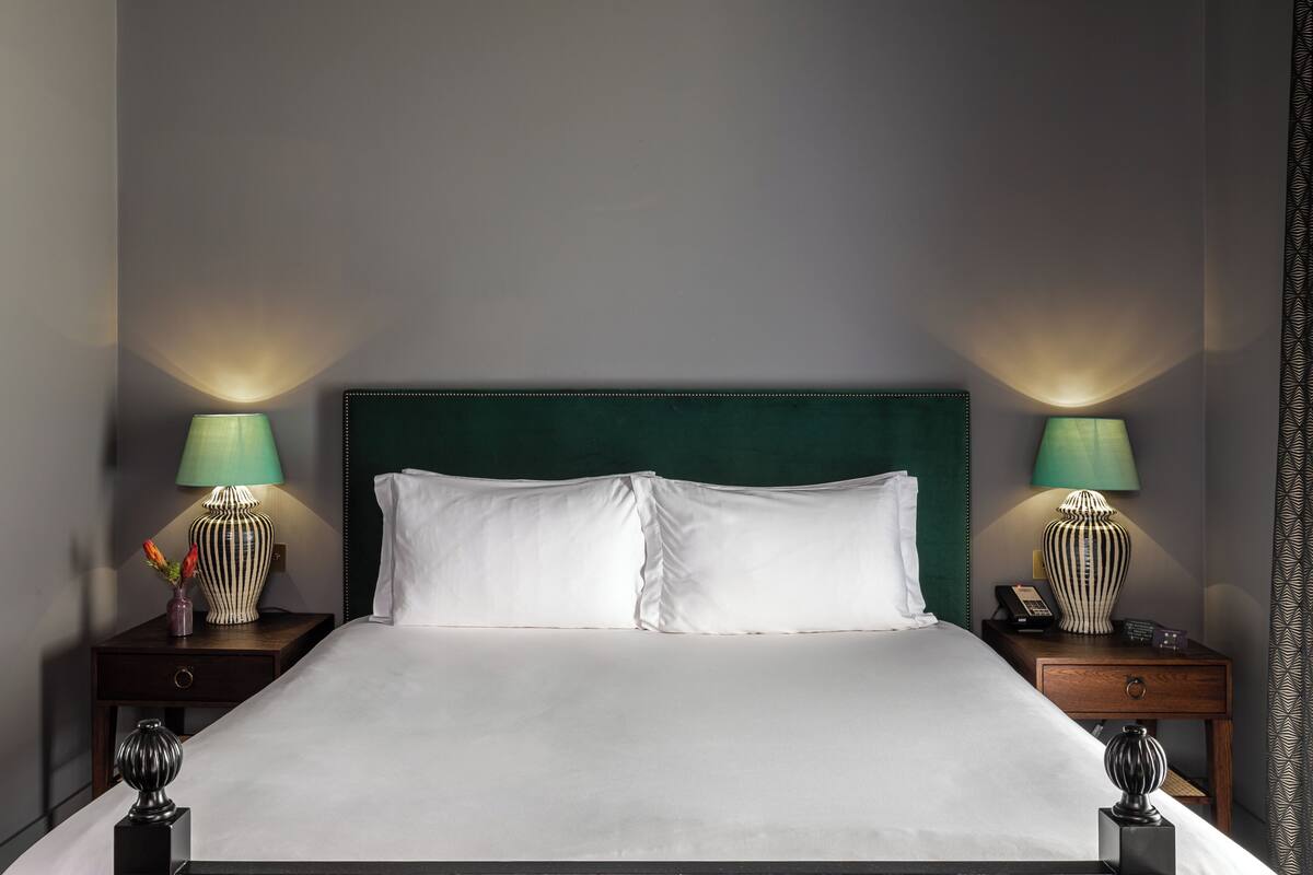 A neatly made bed with a green upholstered headboard, two bedside tables with lamps, and a small vase with flowers on one table.