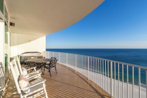 A balcony with a table and chairs, a hot tub, and a view of the ocean.