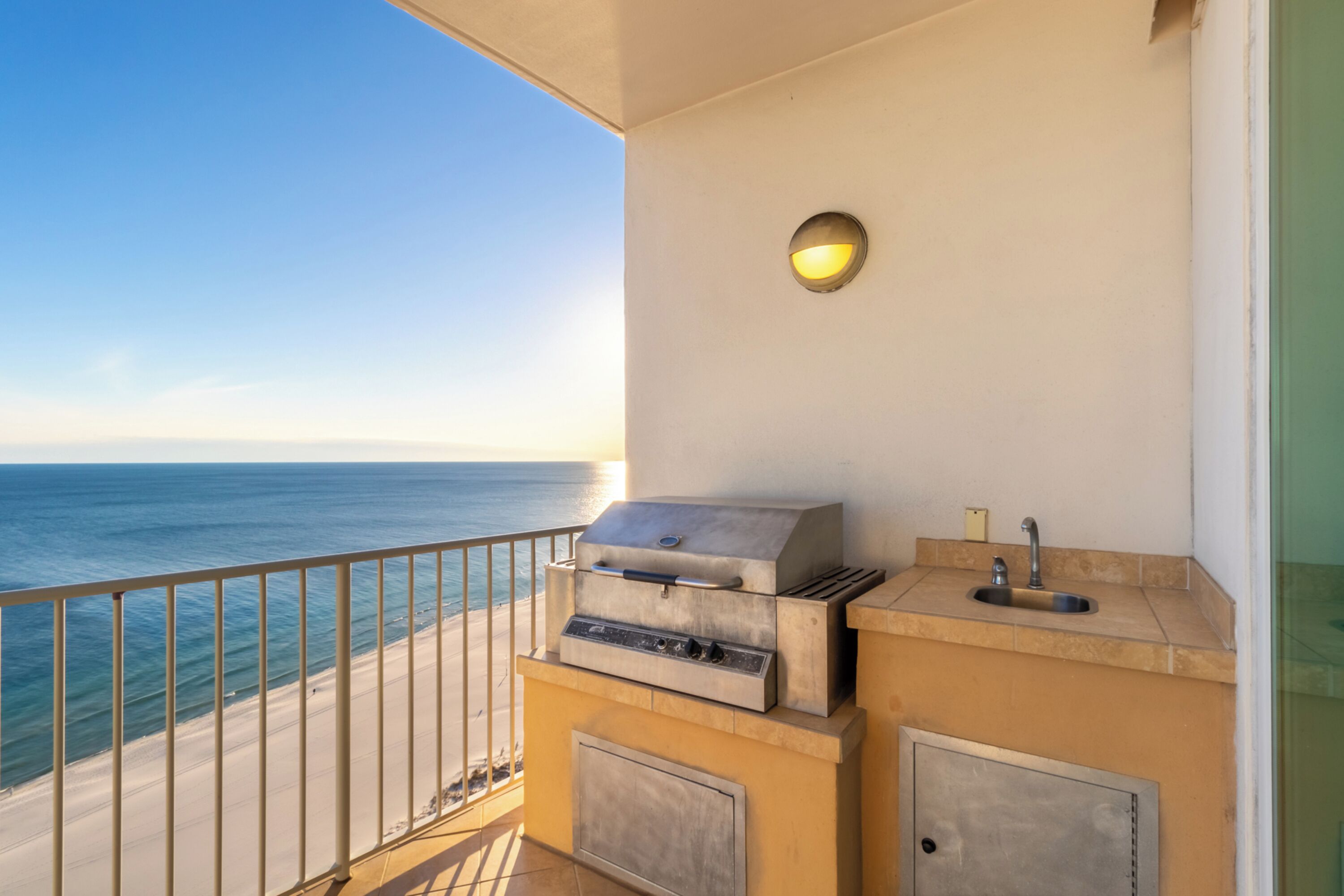 A balcony with a grill, a sink, and a view of the ocean.