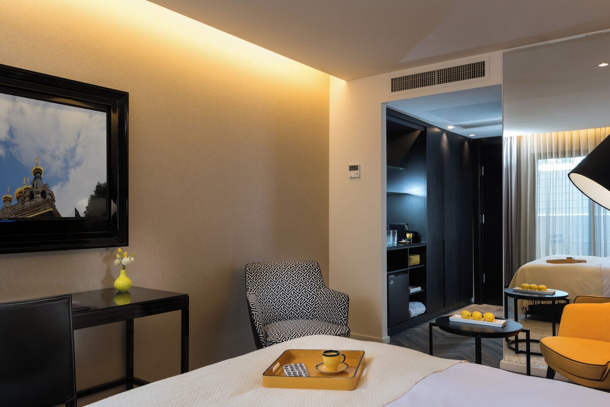 Habitación de hotel con una cama, un escritorio, una silla, una mesita con limones, una bandeja con una taza y un cuadro en la pared.