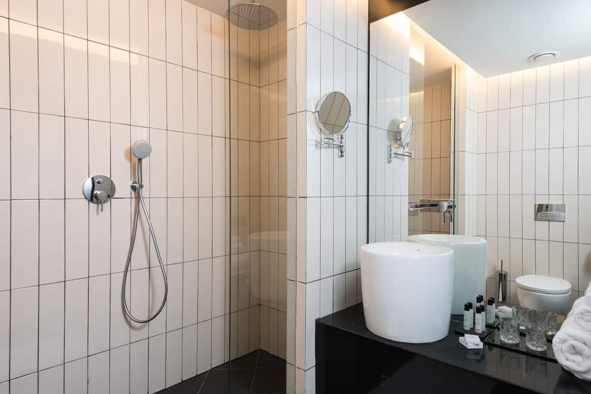 Ein modernes Badezimmer mit weißen Fliesen, einer schwarzen Arbeitsplatte, einem großen Spiegel, einer Duschbrause und zwei Waschbecken.
