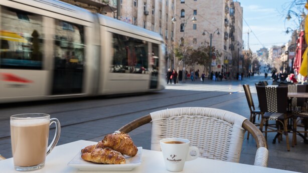 Una mesa con una taza, un plato de pasteles y una silla de mimbre.
