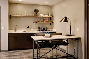 Una cocina compacta con estantes de madera, una mesa de comedor y una lámpara negra.
