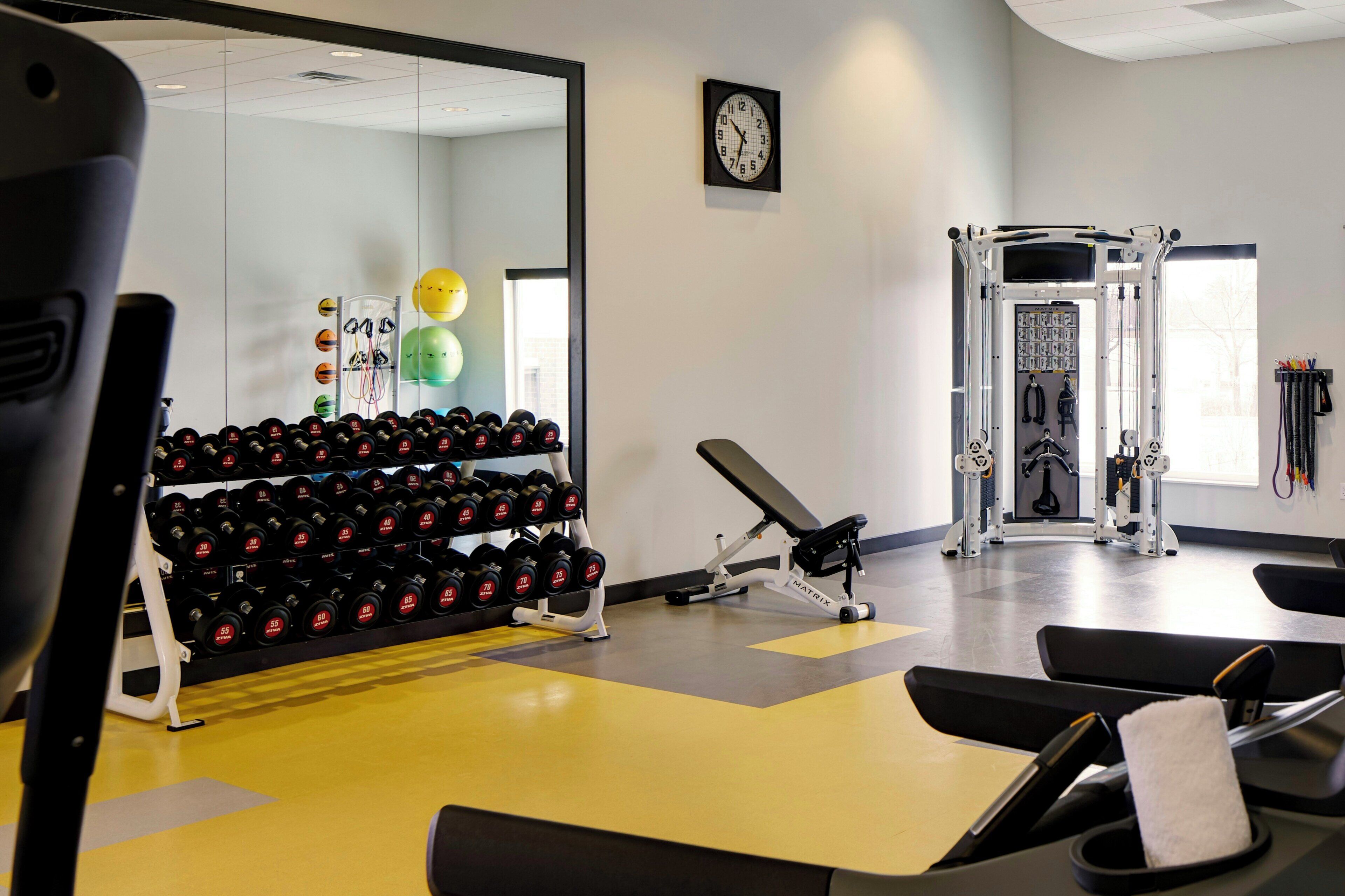 Uma academia com equipamentos de exercício, um espelho e um relógio na parede.