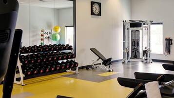 Uma academia com equipamentos de exercício, um espelho e um relógio na parede.