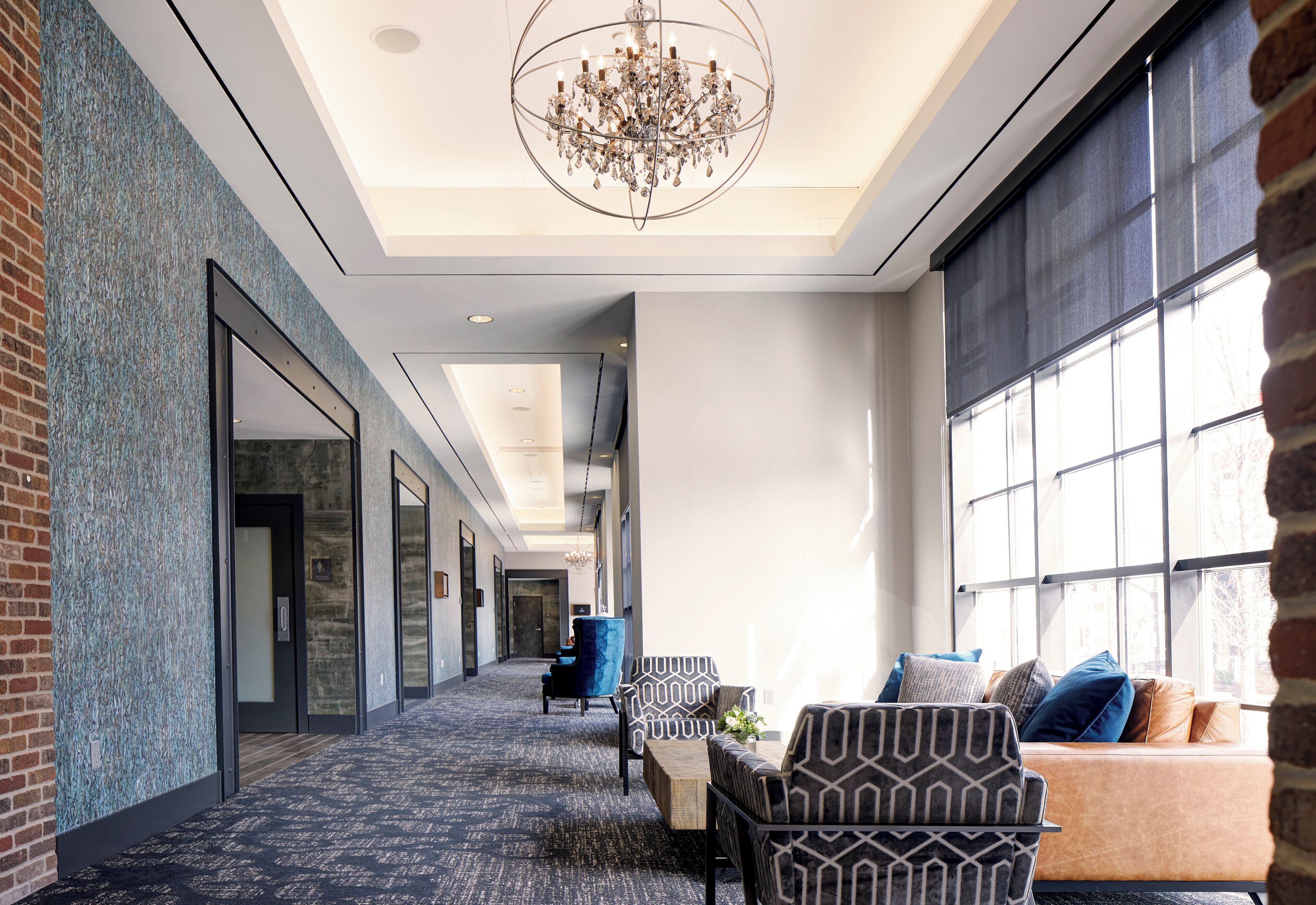 A hotel lobby with a patterned carpet, a chandelier, and a seating area with patterned chairs and a sofa.